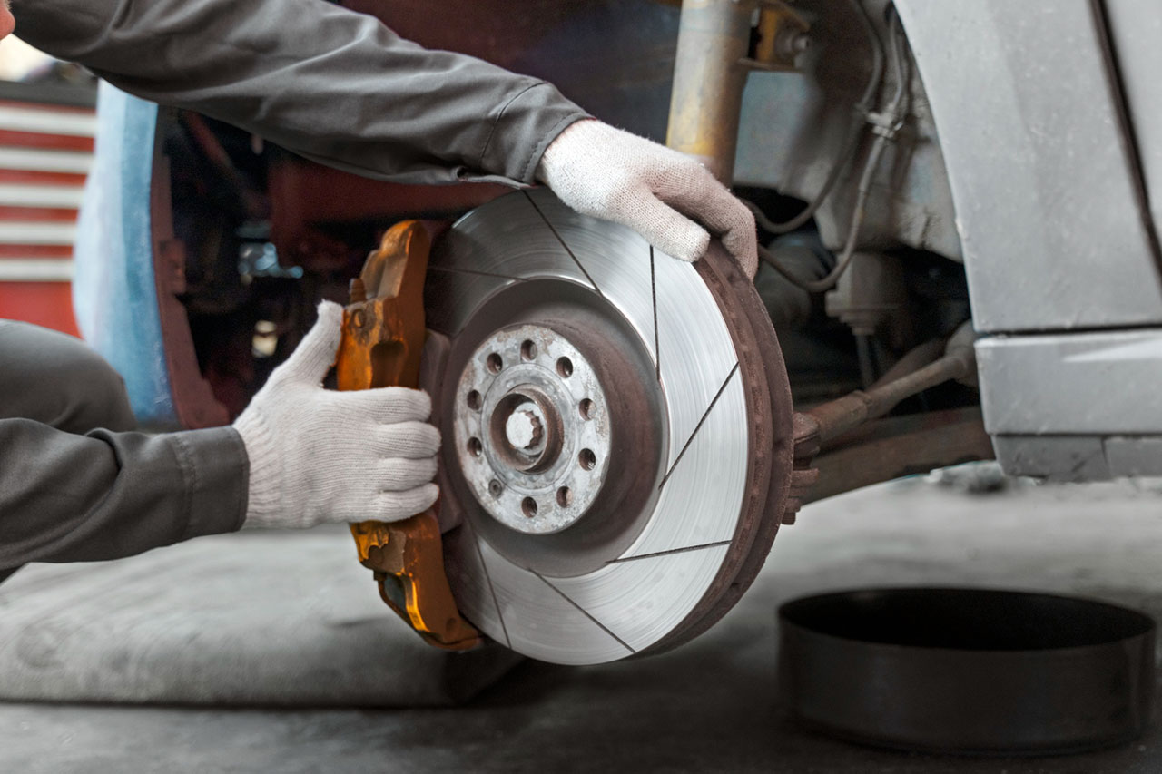 Technician replacing a vehicle brake disc and brake pads during automotive brake repair service