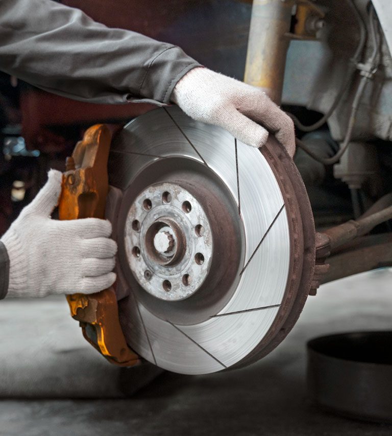 Technician replacing a vehicle brake disc and brake pads during automotive brake repair service